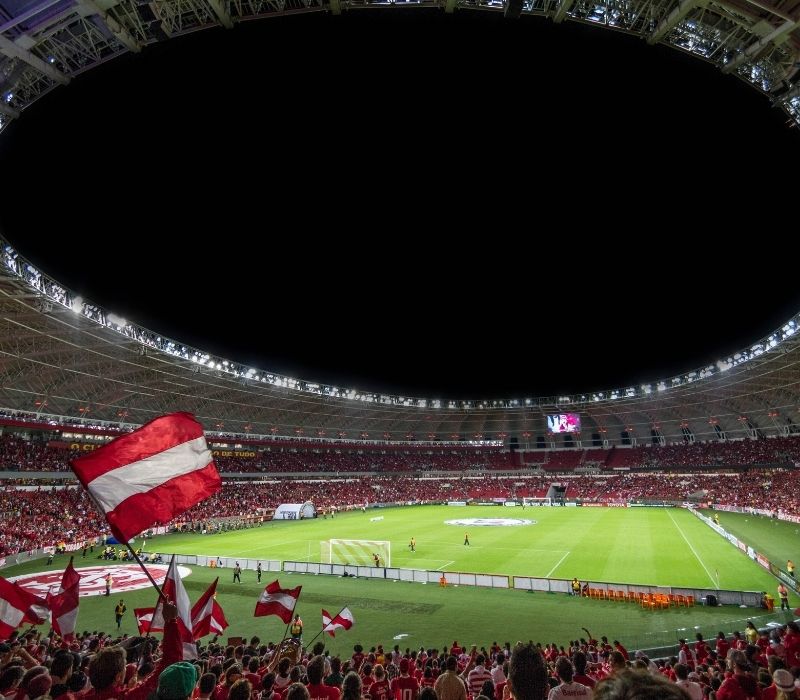 Packed stadium at night with red and white flags waving as fans cheer during a soccer match